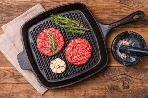 raw burgers from organic beef with garlic and rosemary in a frying pan on an old wooden table, top view